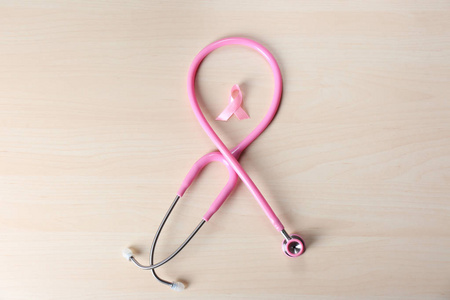 木制背景上带有听诊器的粉红色丝带。 乳腺癌概念