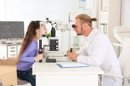 s doctor examining little girl with ophthalmic equipment in clin