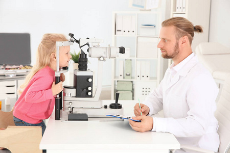 s doctor examining little girl with ophthalmic equipment in clin