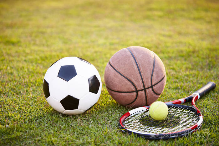 足球足球,足球,篮球,网球,球拍在日落时放在草地上照片-正版商用图片