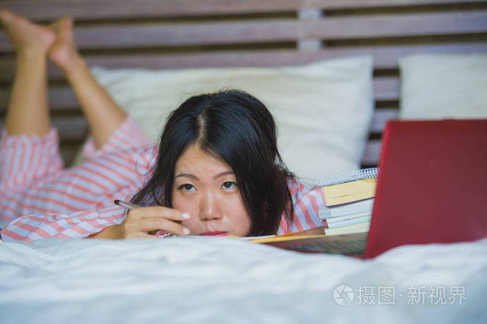 大学生感到无聊和懒惰准备考试用笔记本电脑学习在家卧室里躺在床上