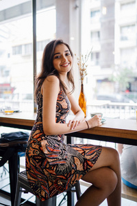 年轻美丽的印度亚洲新加坡女人穿着印花连衣裙坐在咖啡馆里，因为她喜欢在亚洲度过周末。