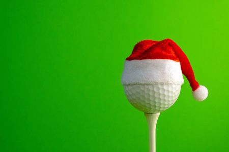 高尔夫球装在一个红色的圣诞老人帽子上。 以圣诞节和新年为主题的体育理念。 复制空间。 绿色背景。