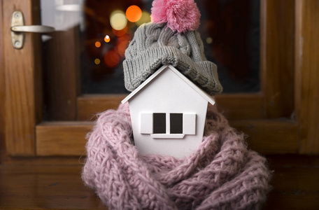 住宅在冬天供暖系统概念和冷的下雪的天气以房子的模型佩带毛线帽