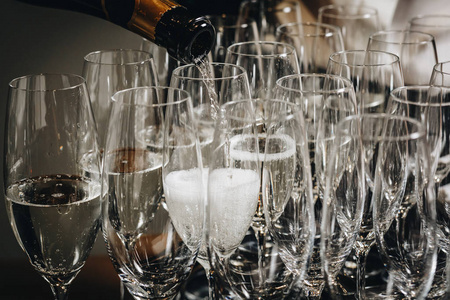 侍者的手在酒杯里倒白葡萄酒或香槟。 把酒倒入玻璃杯中的画面