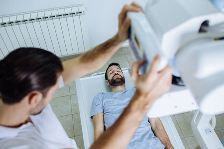 年轻的医疗技术人员操作X光机，而他的病人躺在他面前的床上在一家诊所。