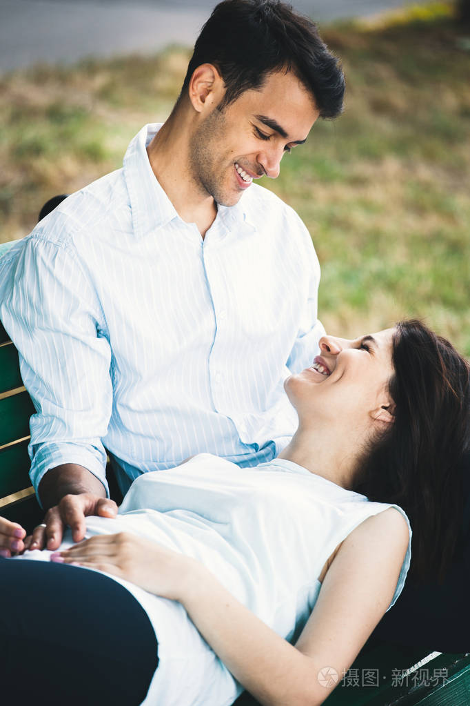 年轻的女人躺在她的男人的膝盖上微笑着看着他快乐的人画像