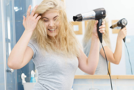 积极的女人在她的金发上使用吹风机。 理发发型的概念。