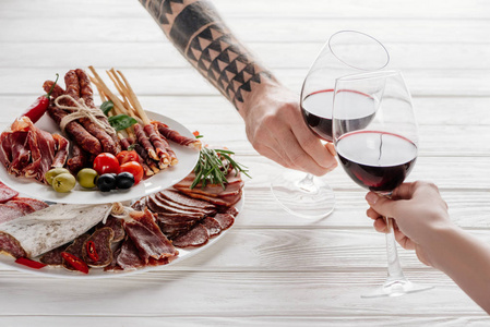 在白色桌面和肉类开胃菜上的带有红酒的两个酒杯的局部视图
