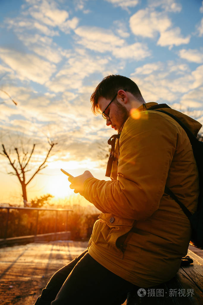 日出时,男人坐在城市公园里,拿着智能手机.生活方式