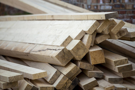 关闭堆积如山的天然棕色凹凸不平的粗糙木板，由明亮的太阳照亮。 用于木工建筑修理和建筑家具木材材料的工业木材。