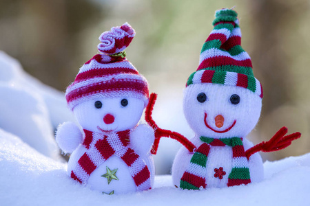 两个小有趣的玩具婴儿雪人在针织帽子和围巾在深雪户外明亮的蓝色和白色复制空间背景。 新年快乐，圣诞贺卡快乐。