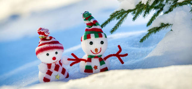 两个小有趣的玩具婴儿雪人在针织帽子和围巾在深雪户外明亮的蓝色和