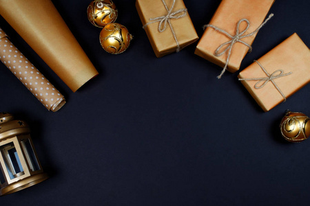 金色闪亮的圣诞鲍布礼物包裹在工艺纸灯笼和黑色背景的包装纸上。 复制空间。 新年和圣诞节庆祝概念。