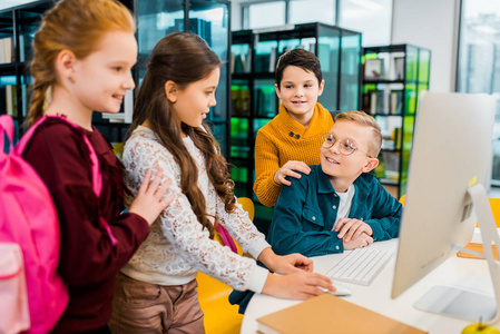 可爱的微笑学童一起使用台式电脑图书馆