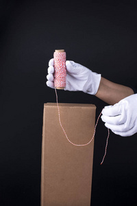 s hands in white gloves pack a gift with a rope of white and red