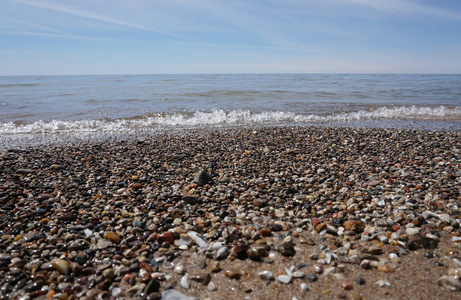 在阳光明媚的日子里，在海滩上的鹅卵石上冲洗海岸线上的水，背景是蓝天