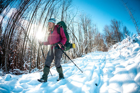 冬天徒步旅行的女人。 一个带着徒步旅行杆背包和雪鞋的女孩正沿着一条积雪的山路行走。 游客沿着森林路走。