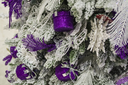 紫色的玩具挂在圣诞树上，上面覆盖着假雪。