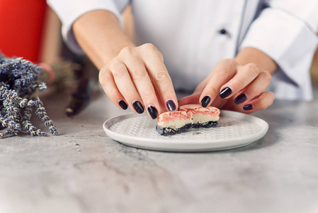 s hands holds a halfcutted pink and gray macaron on a white pla