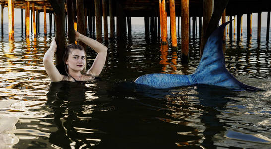 在桥下被乞丐美人鱼在后面的桥下游泳.蓝色的尾巴.身体被鳞片覆盖.