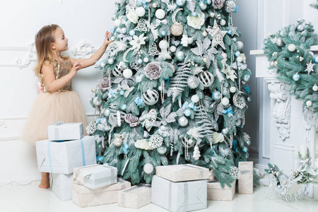 穿着漂亮裙子的小女孩把装饰品挂在圣诞树上。