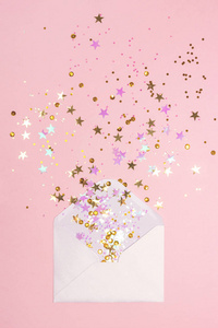 金色和粉红色的五彩纸屑散落在柔和的粉红色背景的信封