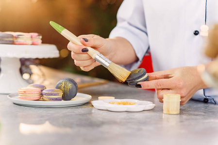 女性糖果油漆与刷金食品法布在一个新鲜的马卡龙。准备刚烤好的马卡龙。