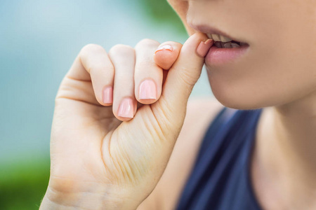 在绿色背景上修指甲的女人手上的钉子断了。女人咬指甲