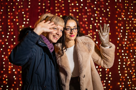 两个有吸引力的女人在圣诞节市场的光墙前摆姿势拍照。
