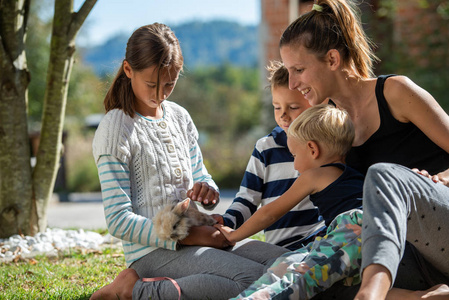快乐的年轻母亲和她的三个孩子在外面享受时间,抚摸他们可爱的宠物