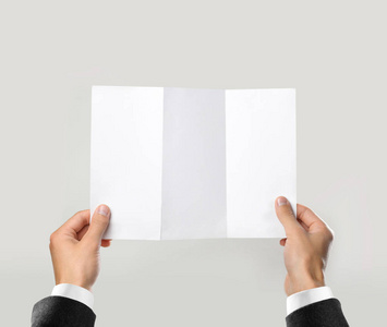 双手穿着白色衬衫和黑色夹克,手里拿着空白的小册子. 单张介绍.