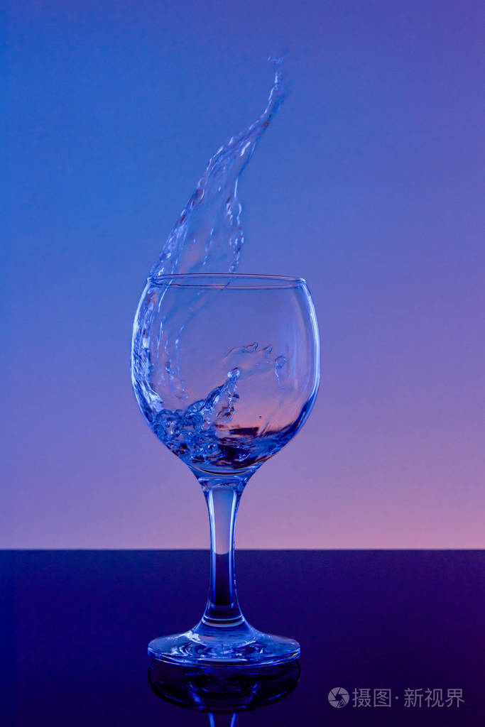 把酒溅在玻璃杯里在蓝色背景上用玻璃喝