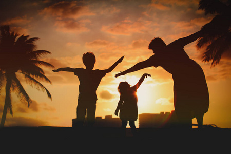 小孩的家庭的剪影在日落海滩玩图片