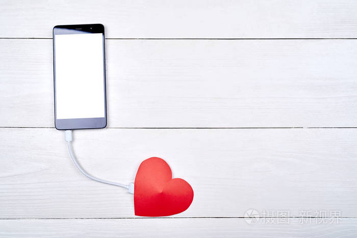 移动智能手机与白色空白屏幕充电与红色纸心在白色木制背景复制空间.