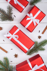 圣诞背景与红色礼品盒，杉树，树枝，肉桂棒和八角。 白色木制背景复制空间上的红色圣诞礼品盒。 节日贺卡。 平躺式顶部视图