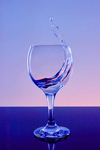 把酒溅在玻璃杯里。 在蓝色背景上用玻璃喝。