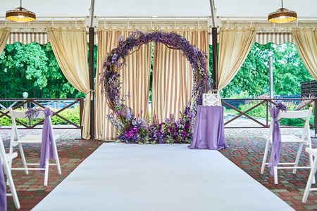 婚礼地点与婚礼拱门装饰紫罗兰花和白色椅子在拱门的每一边户外复制空间。 客人空木椅