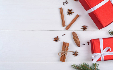 圣诞背景与红色礼品盒，杉树枝，松果，肉桂棒和星星八角在白色的木制背景自由空间。 假日贺卡复印空间。 平躺式顶部视图