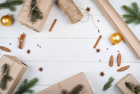 圣诞背景与礼品盒包装牛皮纸冷杉树枝，金色玻璃球，松果，肉桂和八角在白色木制背景自由空间。 平躺式顶部视图