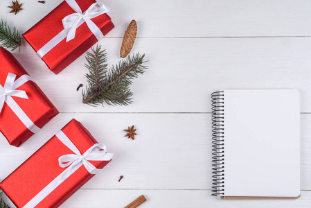 顶部的空白笔记本在白色木制背景与圣诞节装饰复制空间。 圣诞背景与笔记本的愿望清单或做清单红色礼品盒杉树枝。 平躺着