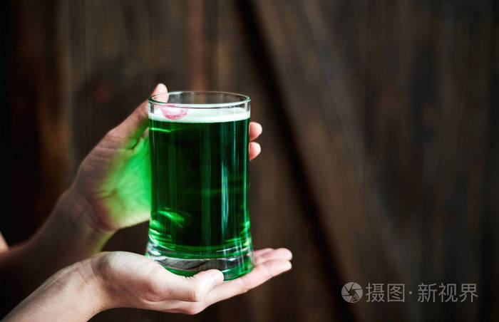 女人拿着绿色啤酒杯,嘴唇印在木制背景复制空间上.