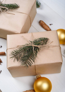 圣诞背景与礼品盒包装牛皮纸冷杉树枝金色玻璃球松果肉桂棒和星星八角白色木制背景