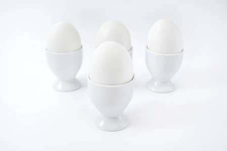 白色鸡蛋站在鸡蛋杯上，分离在白色背景复制空间上。 站着煮鸡蛋。 健康食品概念