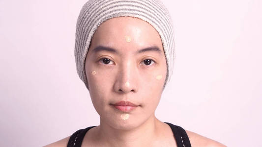 亚洲女孩或妇女，40岁，美丽的脸，日本的外观由粉底液和化妆刷在敏感的皮肤上，帮助她的肤色看起来完美无瑕，真正干瘪。