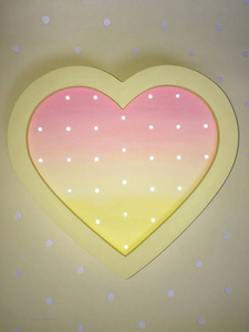 夜光以心脏的形式呈现出微妙的粉红色和黄色。 装饰新生儿卧室的装饰品