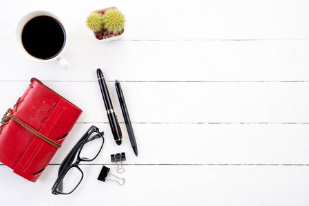 白色木制办公桌桌，配有红色笔记本黑色钢笔咖啡杯等办公用品。 顶部视图与复制空间平躺。
