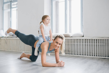 年轻的运动妈妈和女婴一起在健身房锻炼. 亲子健康发展,健身和放松.