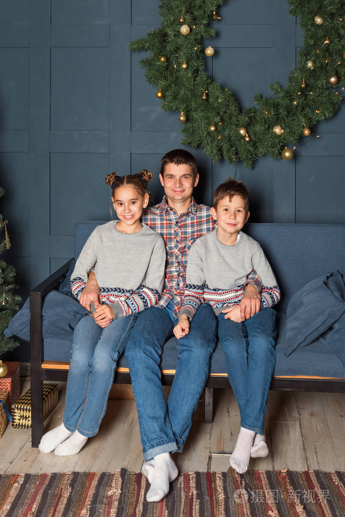 家庭肖像,爸爸带着两个孩子坐在沙发上,在圣诞装饰的房间里微笑着