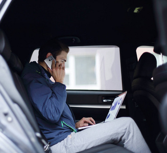 商务人士使用笔记本电脑和手机坐在车里